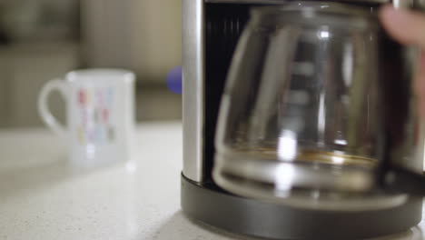 rack focus from coffee mug to woman's hand putting an empty pot into a coffee maker