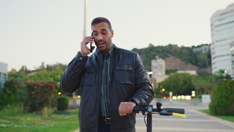 young man with scooter calling on smartphone outdoors.