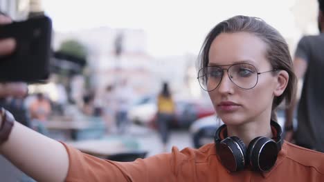 young woman with light day make up standing on the street and taking selfie with her smartphone. blurred street background