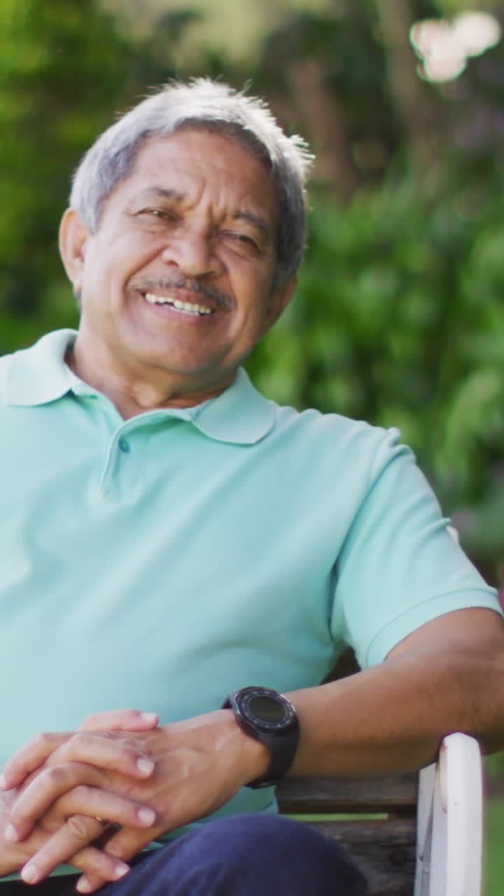 Video of happy biracial senior man sitting on bench in garden