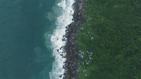 Aerial-zenith-image-captures-the-dynamic-contrast-between-the-ocean-and-the-mountainous-terrain,-where-waves-crash-against-rocky-cliffs