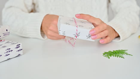 female hands tie the bow of a gift box with wrapping decorated with a pine branch and snowflakes