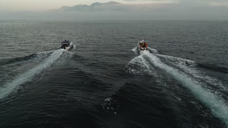 two boats sailing at sunset to an island with a volcano