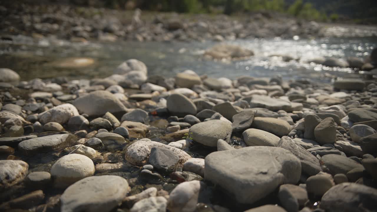 Close-up of smooth river stones along the banks of the Arachthos River in Tzoumerka, with shimmering water in the background. Ideal for themes of nature, tranquility, geology, or outdoor environments.