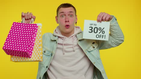 cheerful teen man showing shopping bags and up to 30 percent off inscriptions banner, black friday