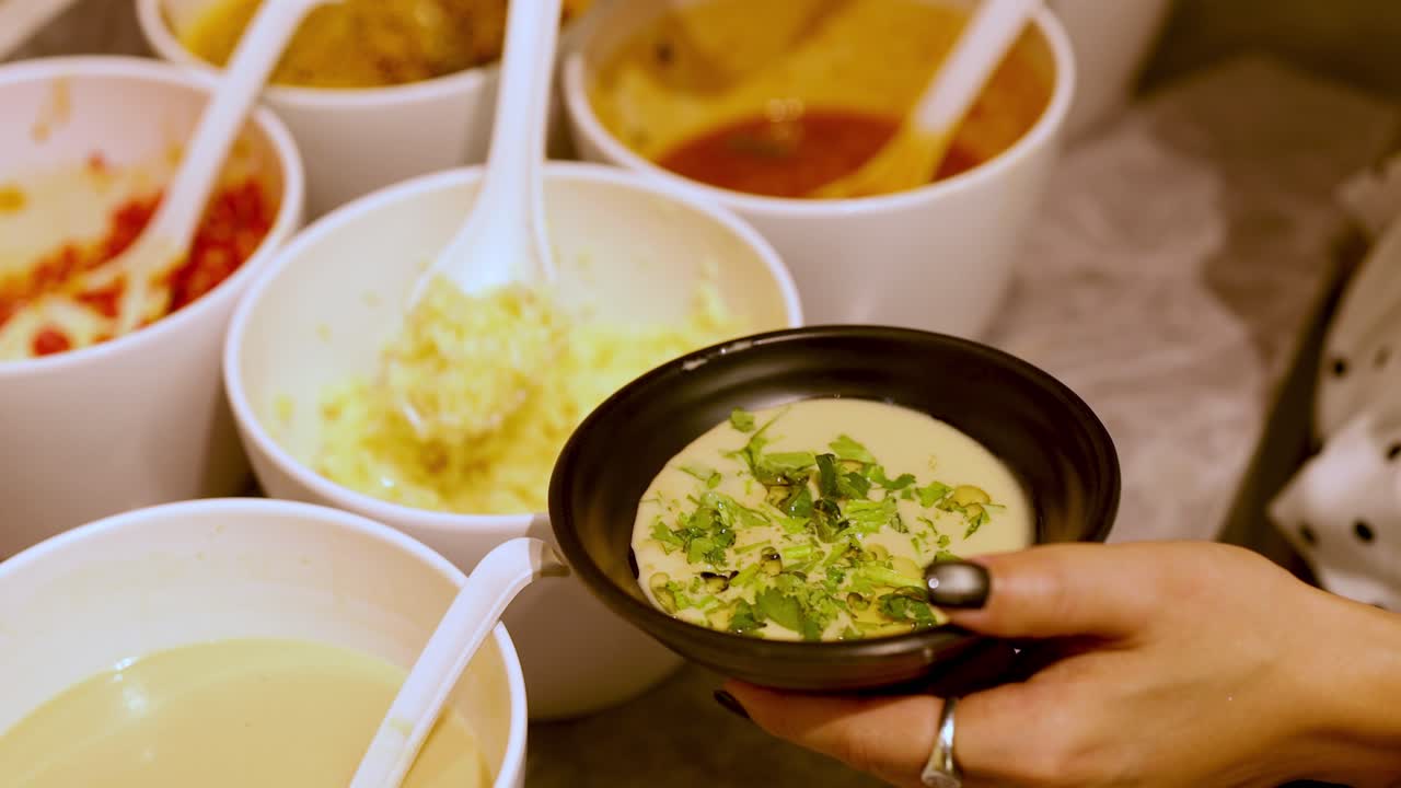 Person adds garlic and herbs to dipping sauce at a well-lit hot pot condiment station