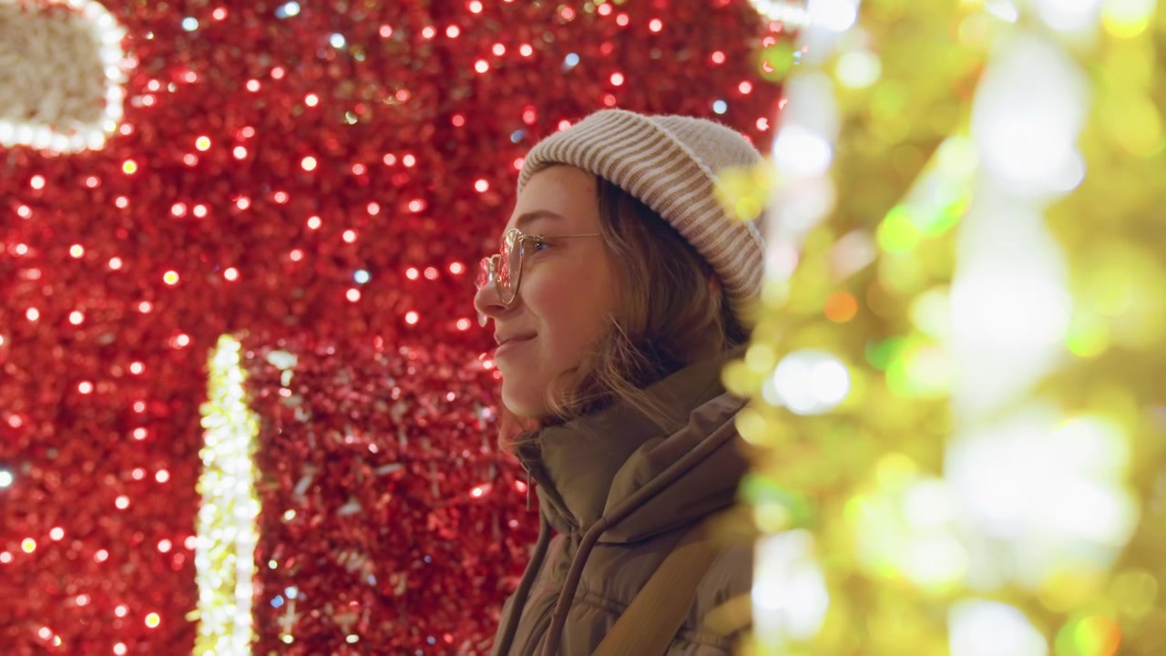 Fondo de purpurina roja, perfil de mujer blanca, compradora urbana navideña con gorro y gafas, deteniéndose a admirar un escaparate iluminado con bokeh dorado en primer plano, chaqueta cómoda, luz baja cinematográfica