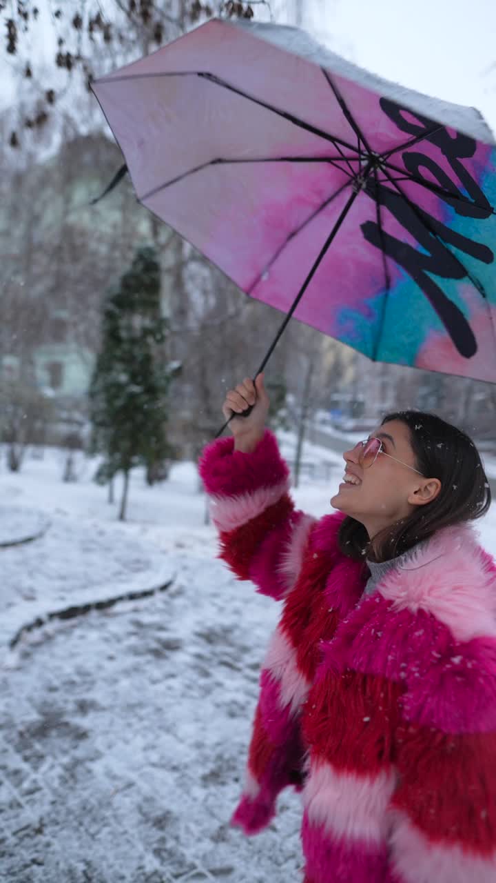mujer con un abrigo de piel rosa en la nieve con un paraguas