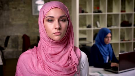 concentrated look og cool middle east woman with serious faces and confident standing position in the brick office, indoor, girls on background