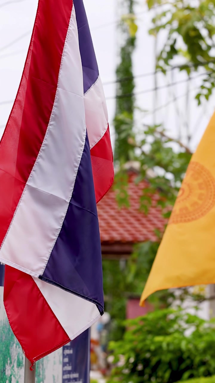Bandiere nazionali thailandesi e buddiste gialle sventolano dolcemente nella brezza vicino all'ingresso di un tempio.