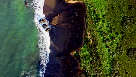 volando sobre olas iluminadas por el sol y playa de arena tallada en altos acantilados en california