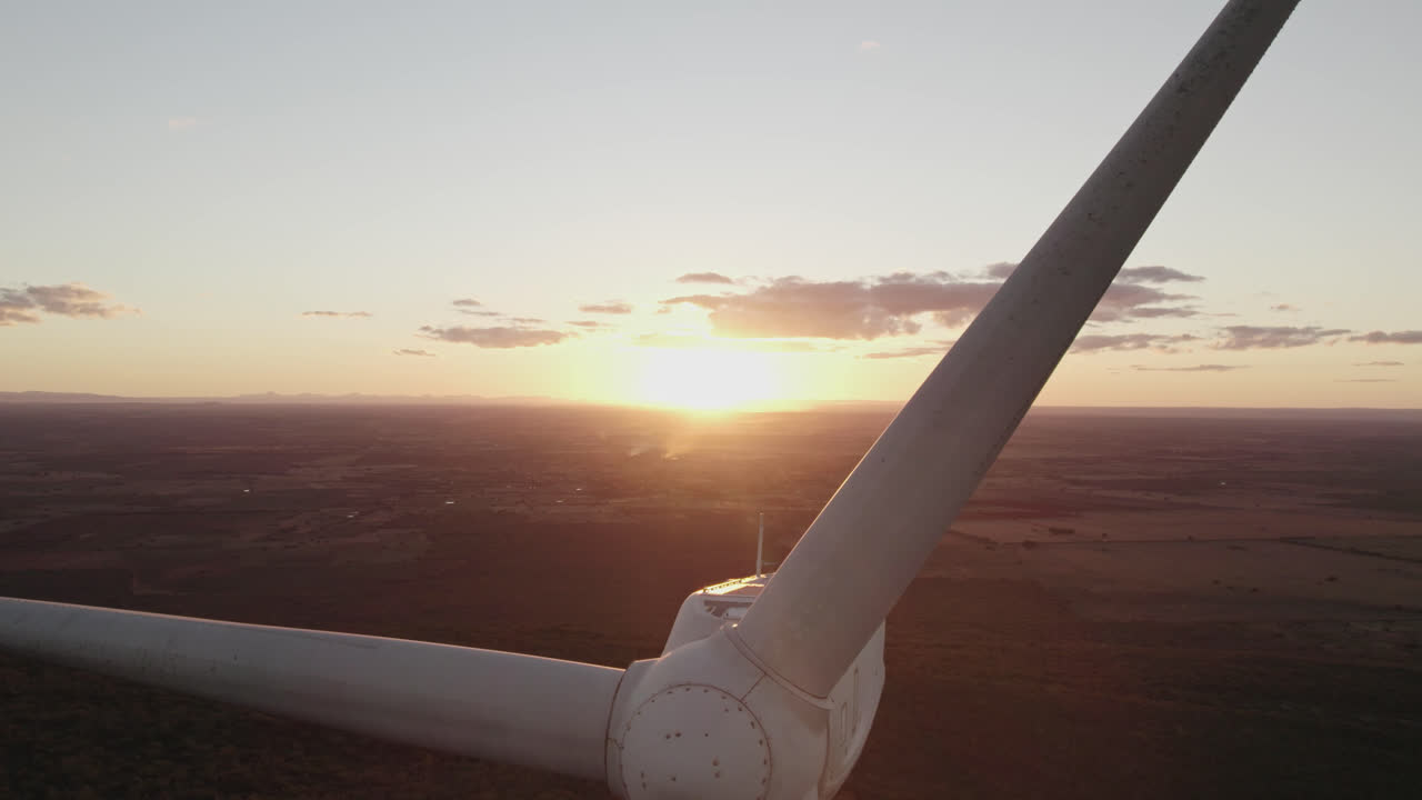 Revealing Aerial shot rising near stopped wind turbine, sunset in background. Close up
