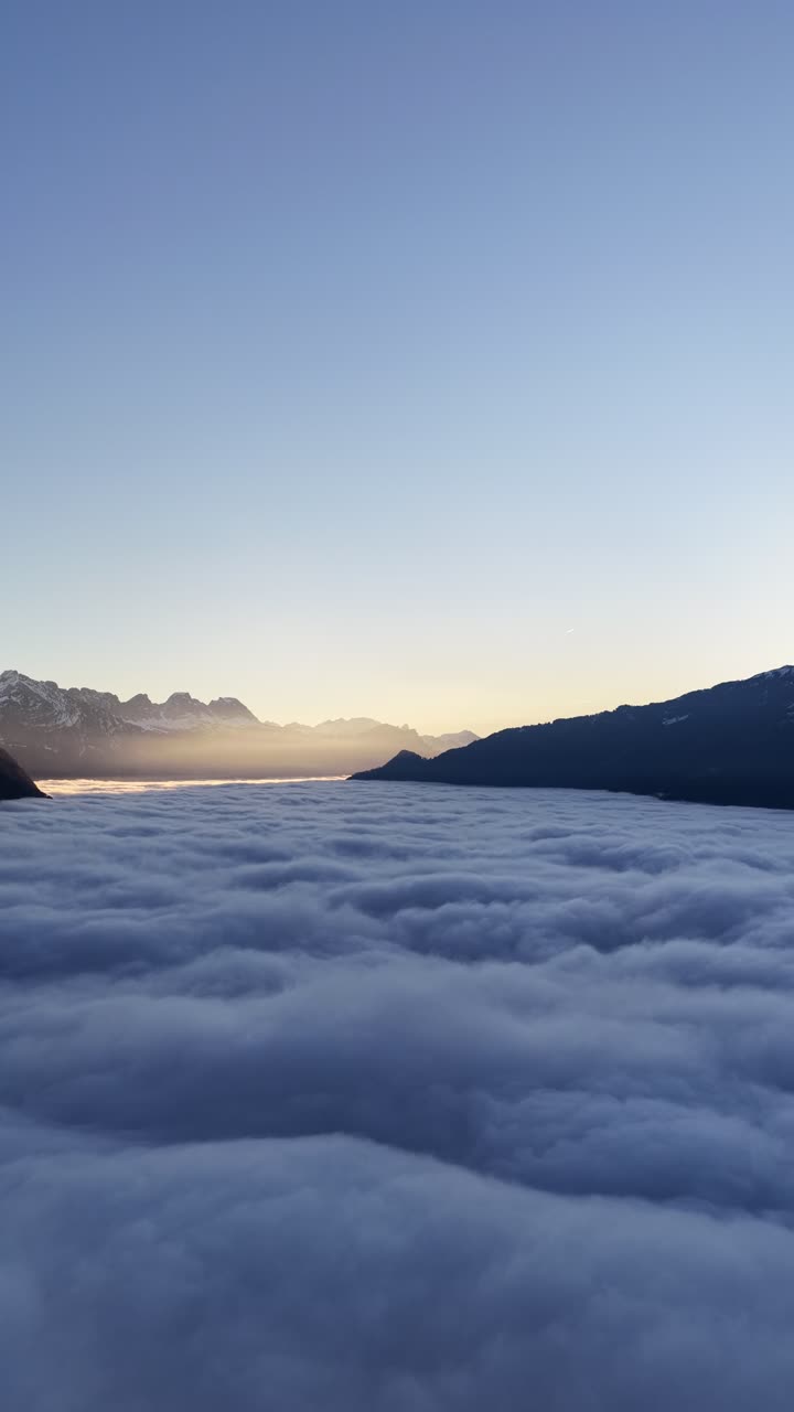 Nuvole dense avvolgono una valle di montagna all'alba con luce soffusa sulle cime innevate