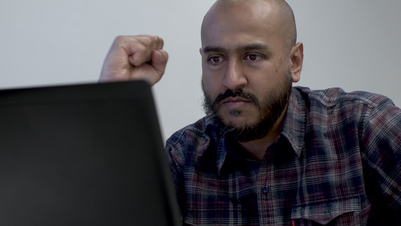 An Indian man celebrating with a fist pump as he reads the content of an email, satisfied with the good news and happy as he has won an important client pitch