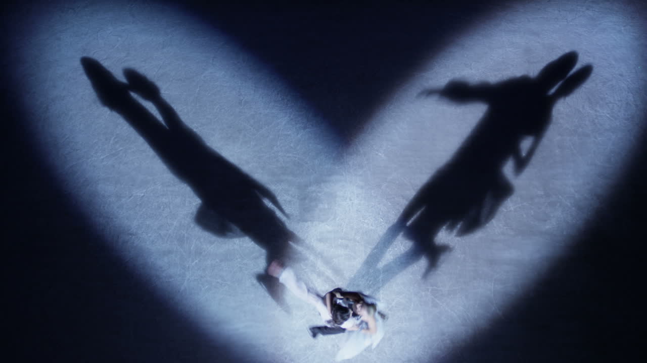 피겨 스케이팅 선수 들 이 스포트라이트 에서 사랑 의 춤 을 연주 하고 있다