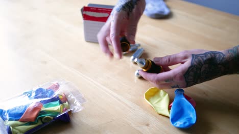 un joven con tatuajes está soplando un globo colorido con óxido nitroso a través de un dispositivo de craqueo de gas