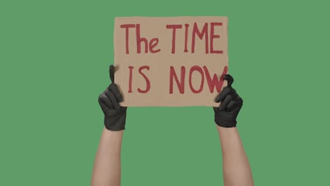 female hands in black gloves pick up a poster from a cardboard box that reads the time is now. cardboard banner. isolated a green screen, chroma key. close up. slow motion