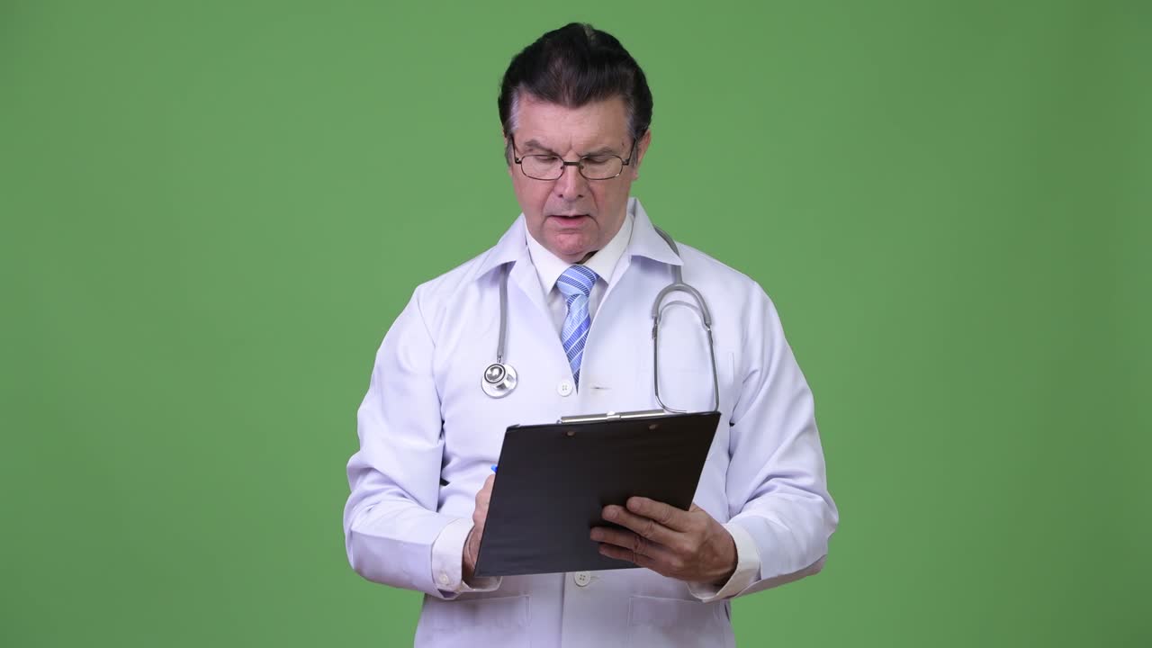Senior handsome man doctor consulting while writing on clipboard