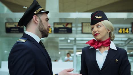 in airport stewardess with blond hair smiling affably, talking with pilot. european woman dressed in dark blue uniform, scarlet red scarf tied on her white shirt. cinematic shot on red camera. 2 models.