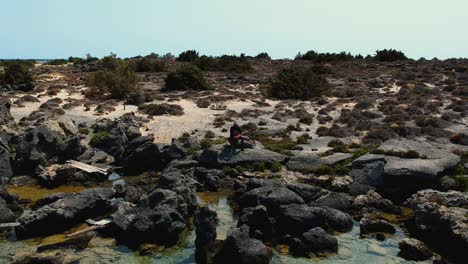 Toma-Panorámica-Con-Drones-De-Una-Modelo-Sentada-En-Una-Increíble-Playa-De-Isla-Paradisíaca-Elafonissi,-Creta