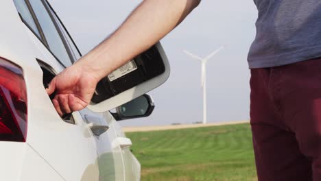 opening car gas tank cap, windmill in background, change from fossil fuel to electric power