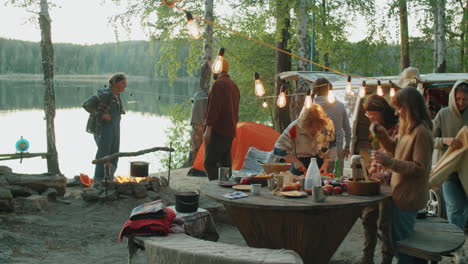 amigos jóvenes preparando comida en el campamento junto al lago