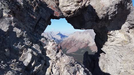 Hiker-on-rock-arch-view-trough-hole-on-Mountain-tilt-Kananaskis-Alberta-Canada