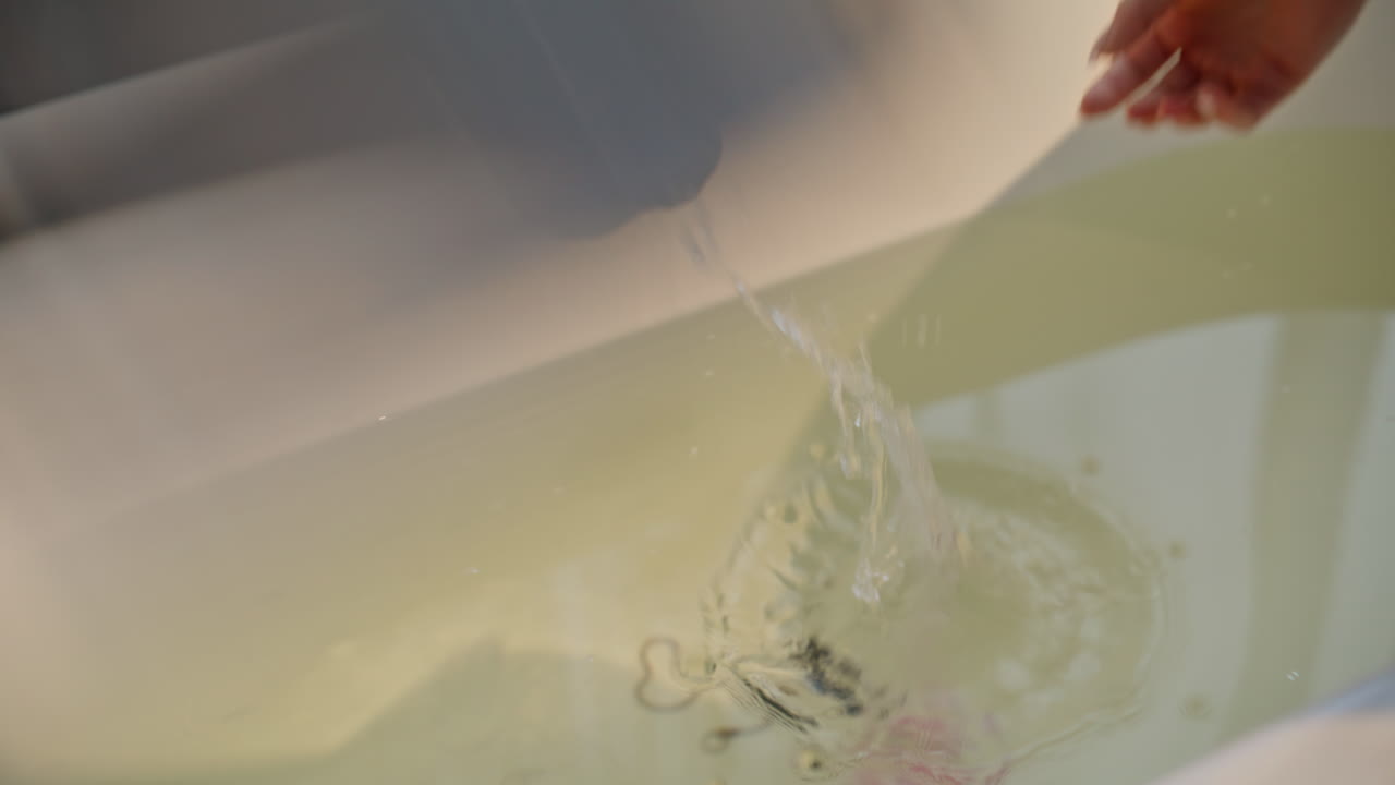 Una mano prende una bomba da bagno e la mette nell'acqua. Una donna prepara una vasca da bagno schiumosa.