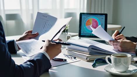 two people are sitting at a table with papers and laptops