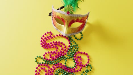 Vídeo-De-Máscara-De-Mascarada-Con-Plumas-Y-Cuentas-De-Mardi-Gras-Sobre-Fondo-Amarillo-Con-Espacio-Para-Copiar