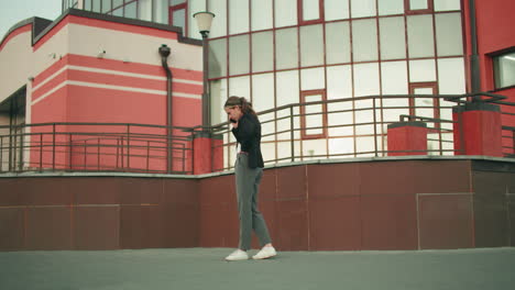 tense young adult pacing on phone call near fence in urban area, appearing stressed while engaged in conversation, wearing formal attire in modern setting