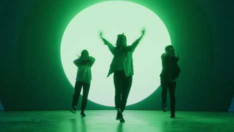 diverse group of three professional dancers performing a hip hop dance routine in front of big led wall screen with green vfx animation during a virtual production in studio environment. 105 bpm song.