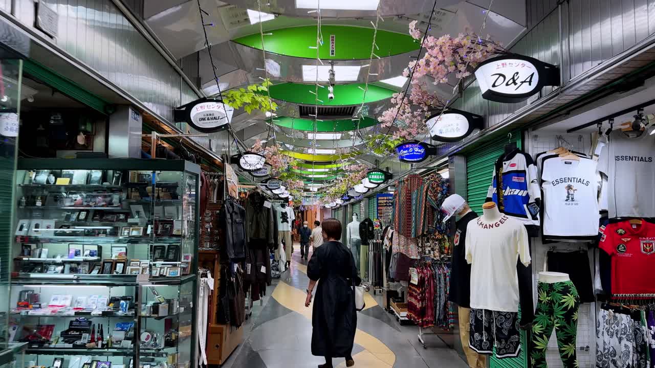 A person walks through a quiet, covered market with green shutters and colorful lights overhead