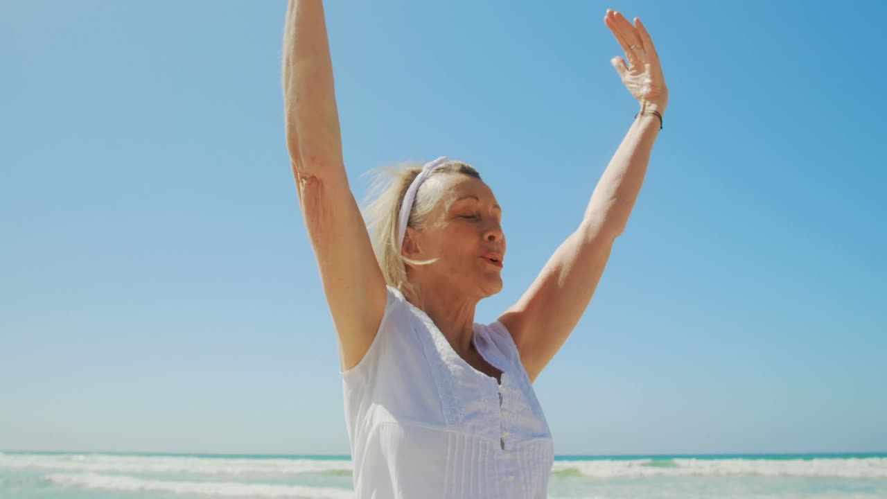 vista frontal de una mujer caucásica senior activa realizando yoga en la playa 4k
