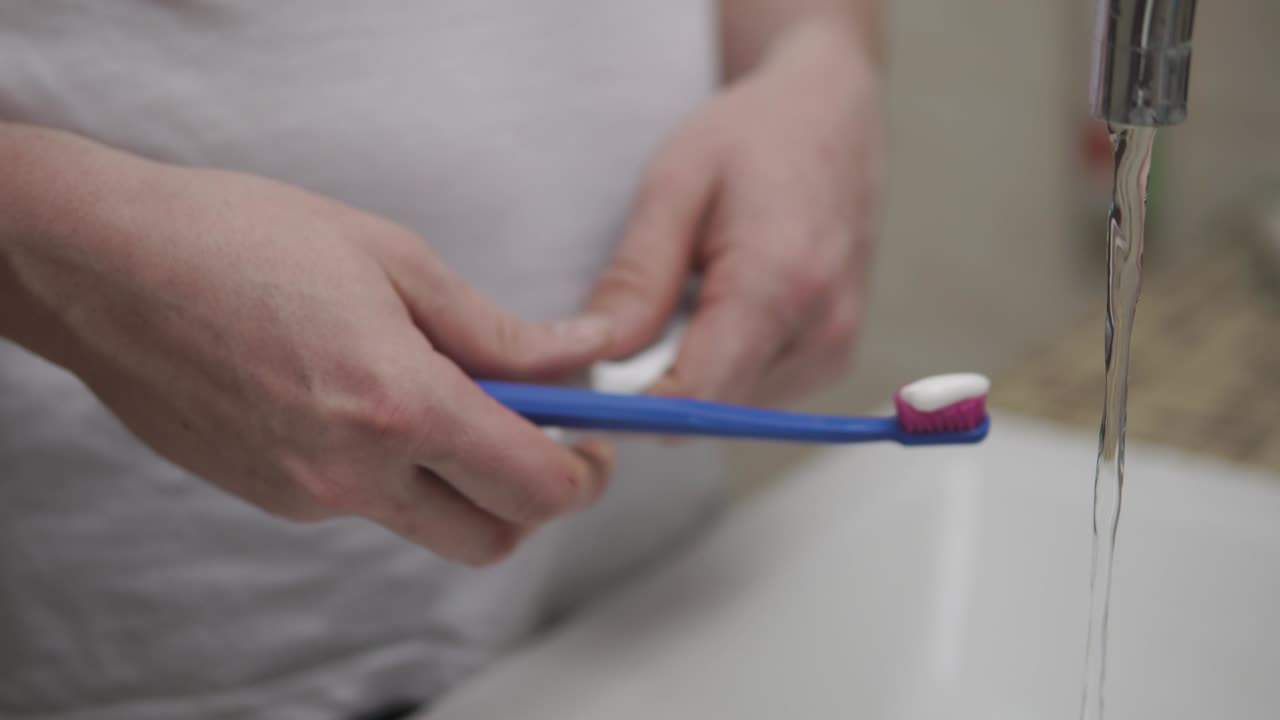 fotografía de las manos de un hombre, que está aplicando pasta de dientes en un cepillo y cepillando los dientes