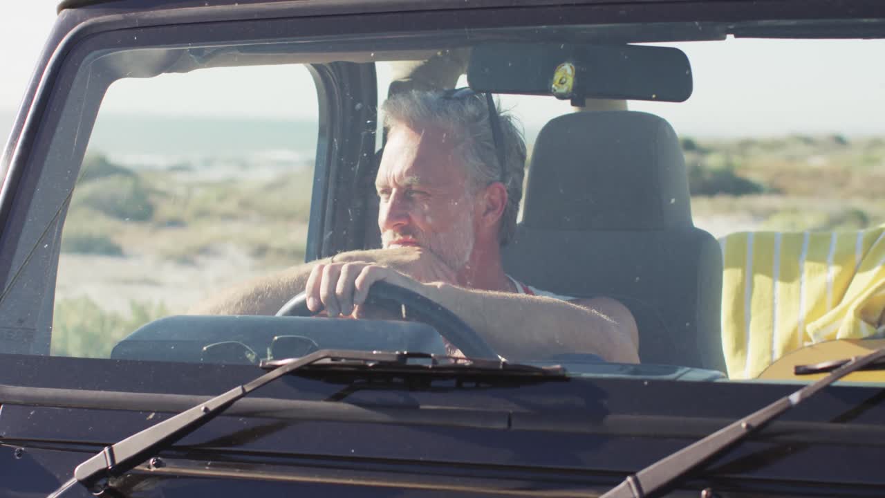 Uomo caucasico pensieroso seduto in auto che guarda altrove in una giornata di sole in spiaggia.
