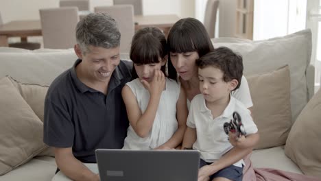 padres felices y dos hijos sentados en la computadora portátil en la sala de estar