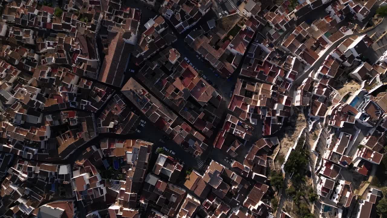 drone shot of Canillas de Aceituno in spain during midday. We see small streets in an old cramped city. There is not much action on the street. The drone makes an upwards and yawing motion.