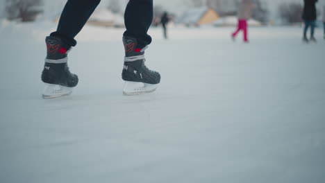 lower angle view of person skillfully skating on smooth frozen ice with blurred skaters in background under pale winter sky capturing motion and grace in cold outdoor scene soft light