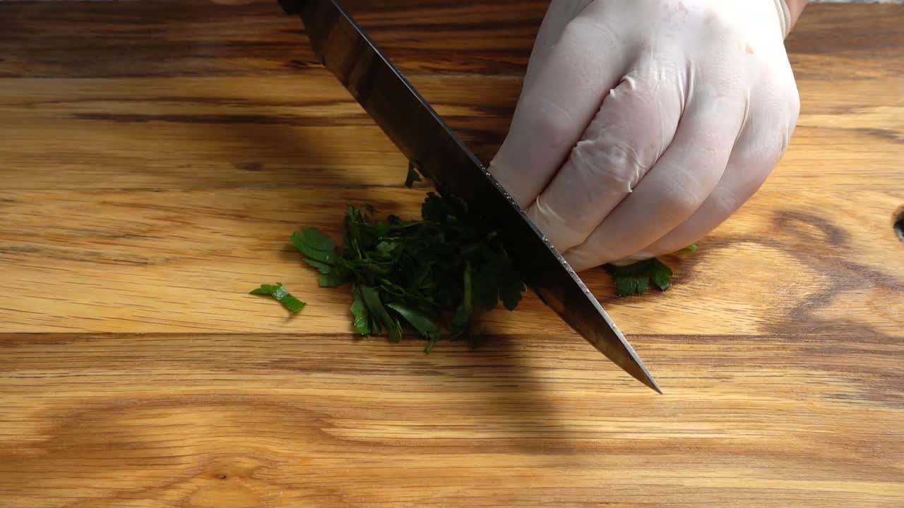 Chef chopping parsley leaves with a knife on a cutting board