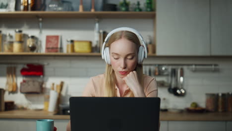 girl student listening online lesson sitting with headphones at kitchen close up