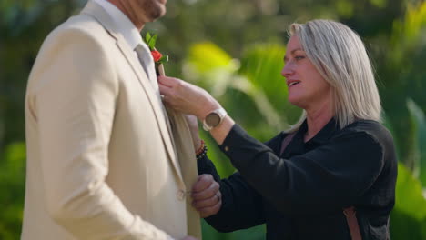 close up blonde woman primping groom in beige suit for wedding day, 4k slow motion