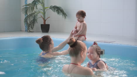 happy middle-aged mother swimming with cute adorable baby in swimming pool. smiling mom and little child, newborn girl having fun together. active family spending leisure and time in spa hotel.