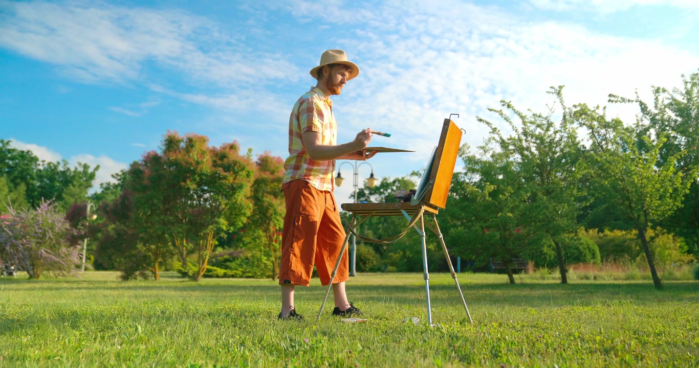 晴れた公園でイーゼルに絵を描く帽子をかぶった男性