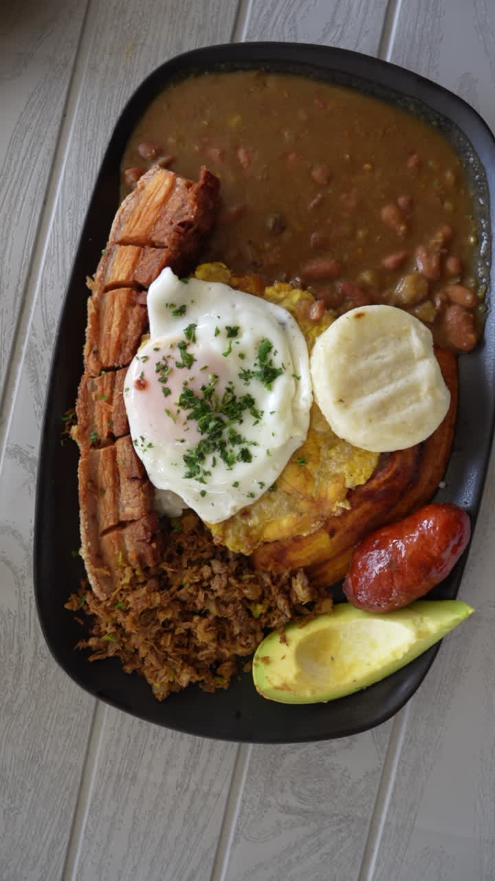 Close-up shot of Bandeja Paisa on a wooden table. Colombian dish with beans, rice, chicharrón, egg, and arepa showcased beautifully in vertical video for mobile and social media