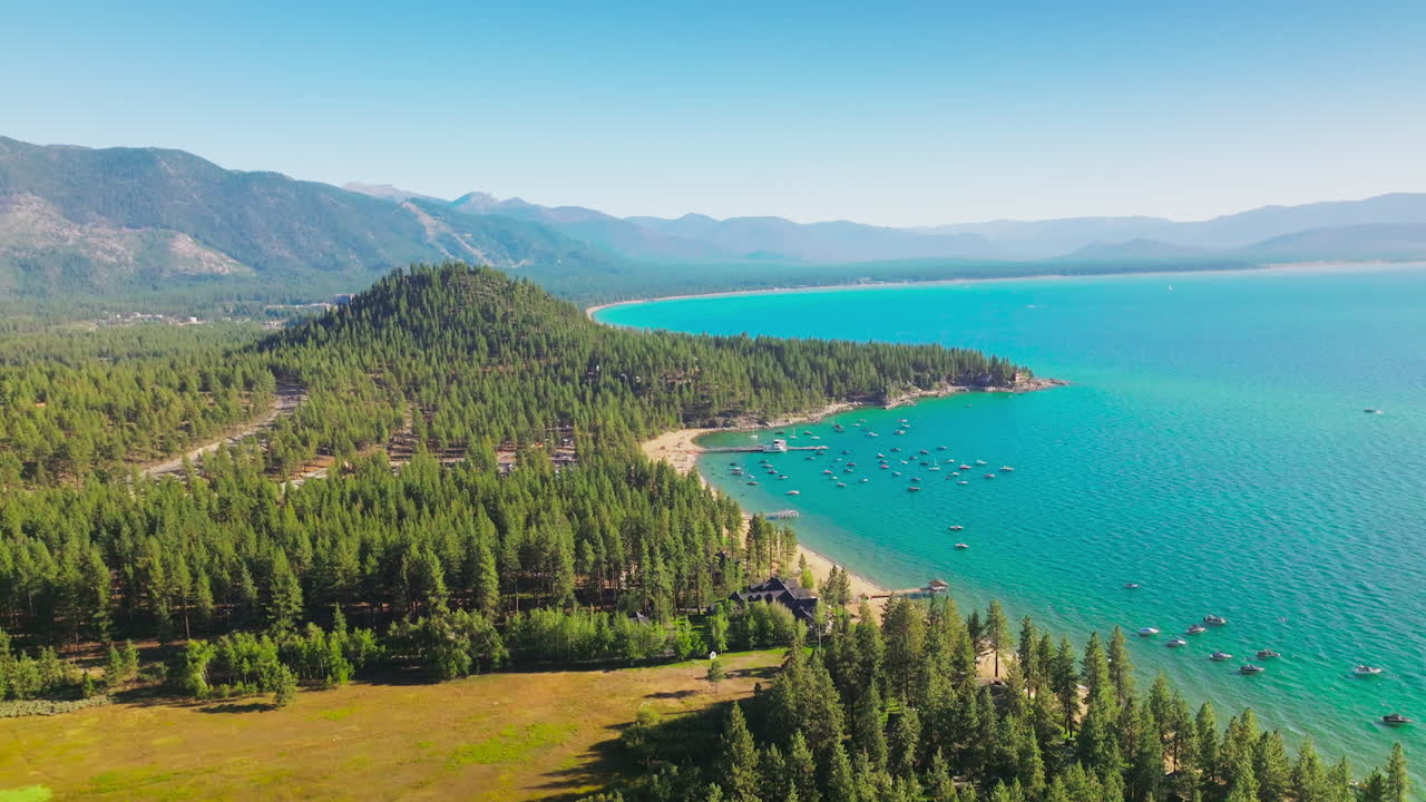 Amazingly turquoise color of the Lake Tahoe with lots of boats at the shore. Resort area locating in the pine tree forest. Mountains surrounding the lake.