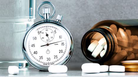 chronometer stopwatch with medicine pills and vitamine bottle on gray background