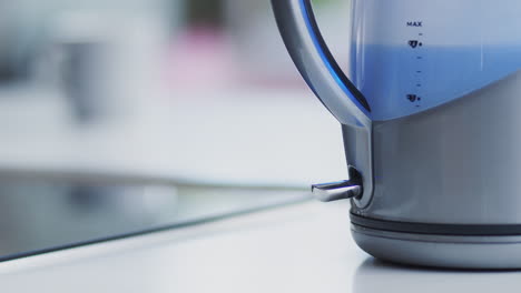 close up of woman pressing power switch to boil electric kettle at home