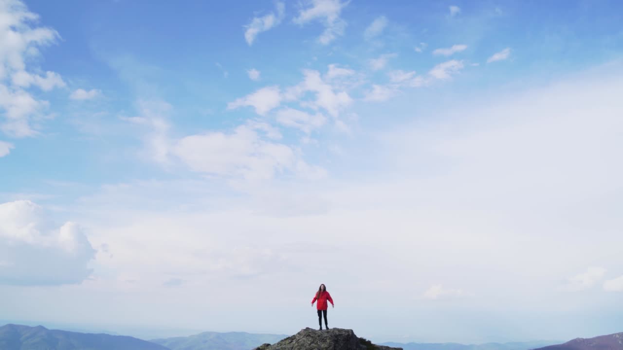 Young woman stands on a mountain summit with arms lifted toward the sky, embracing freedom, success, and connection with nature. A powerful visual of victory and personal triumph