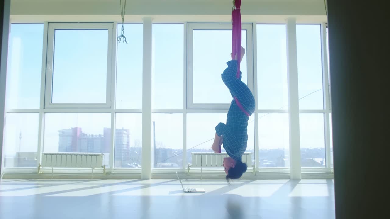 Woman practicing aerial yoga with a laptop